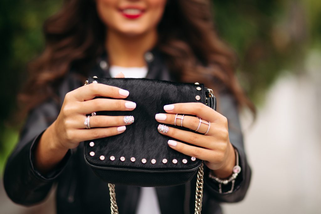 girl with manicured nails with beautiful ornament wedding rings holding black fur bag